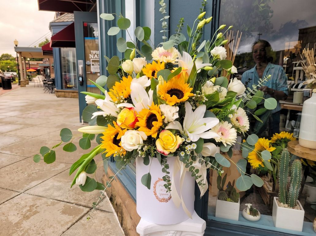 White floral arrangement with yellow sunflowers in a planter outside a storefront window