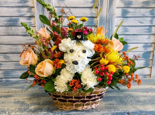 Floral basket with white dog made of flowers, surrounded by peach, yellow, and orange blooms