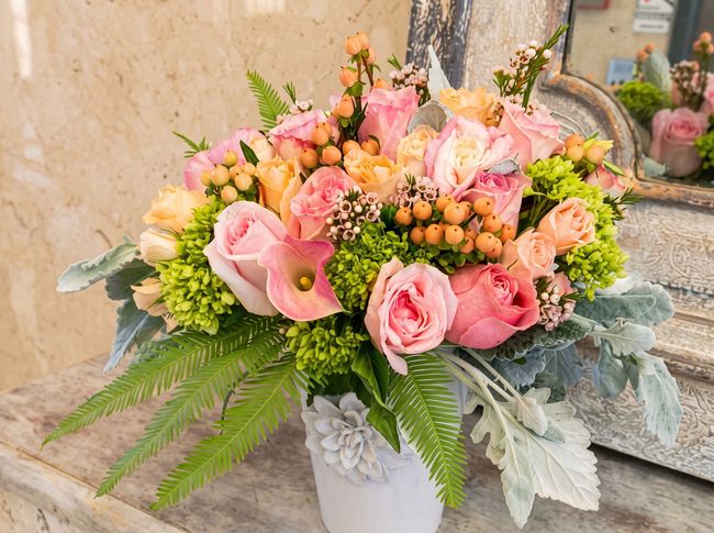 Pink and peach floral arrangement in a white vase with greenery on a table