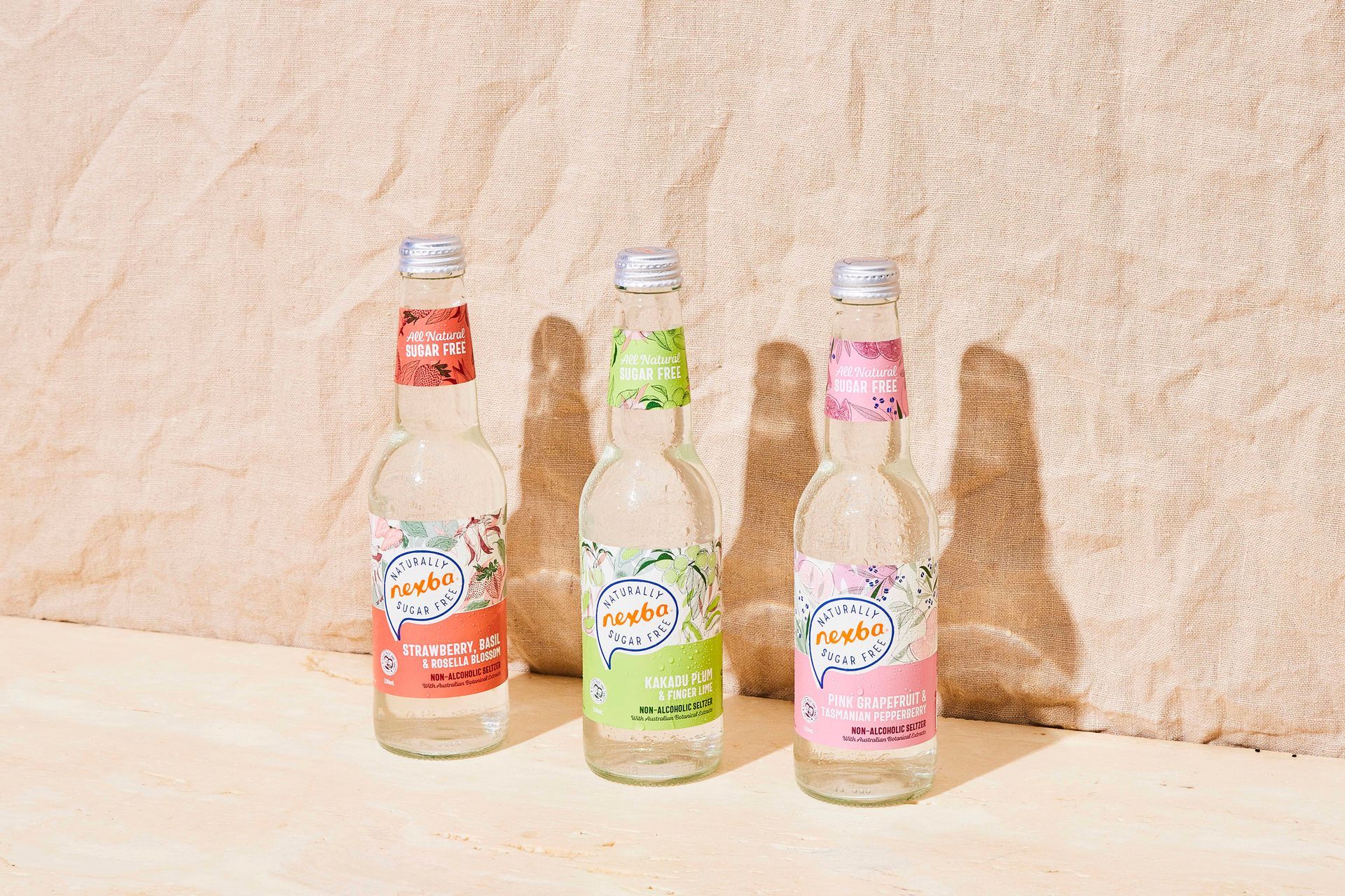 Three bottled drinks with colorful labels on a sunlit wooden surface