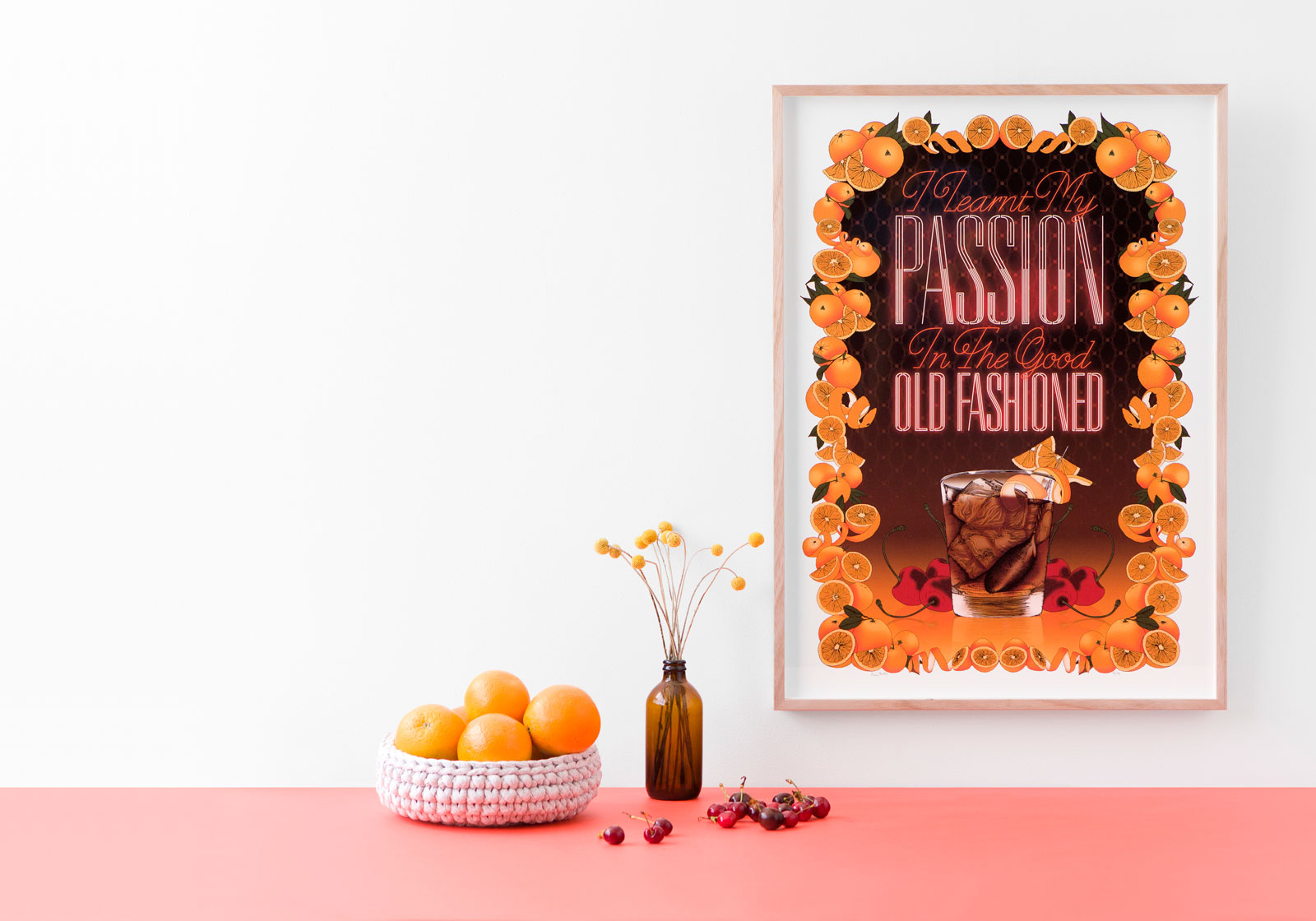 Framed orange floral “PASSION” poster on a white wall above a pink tabletop with oranges and a vase