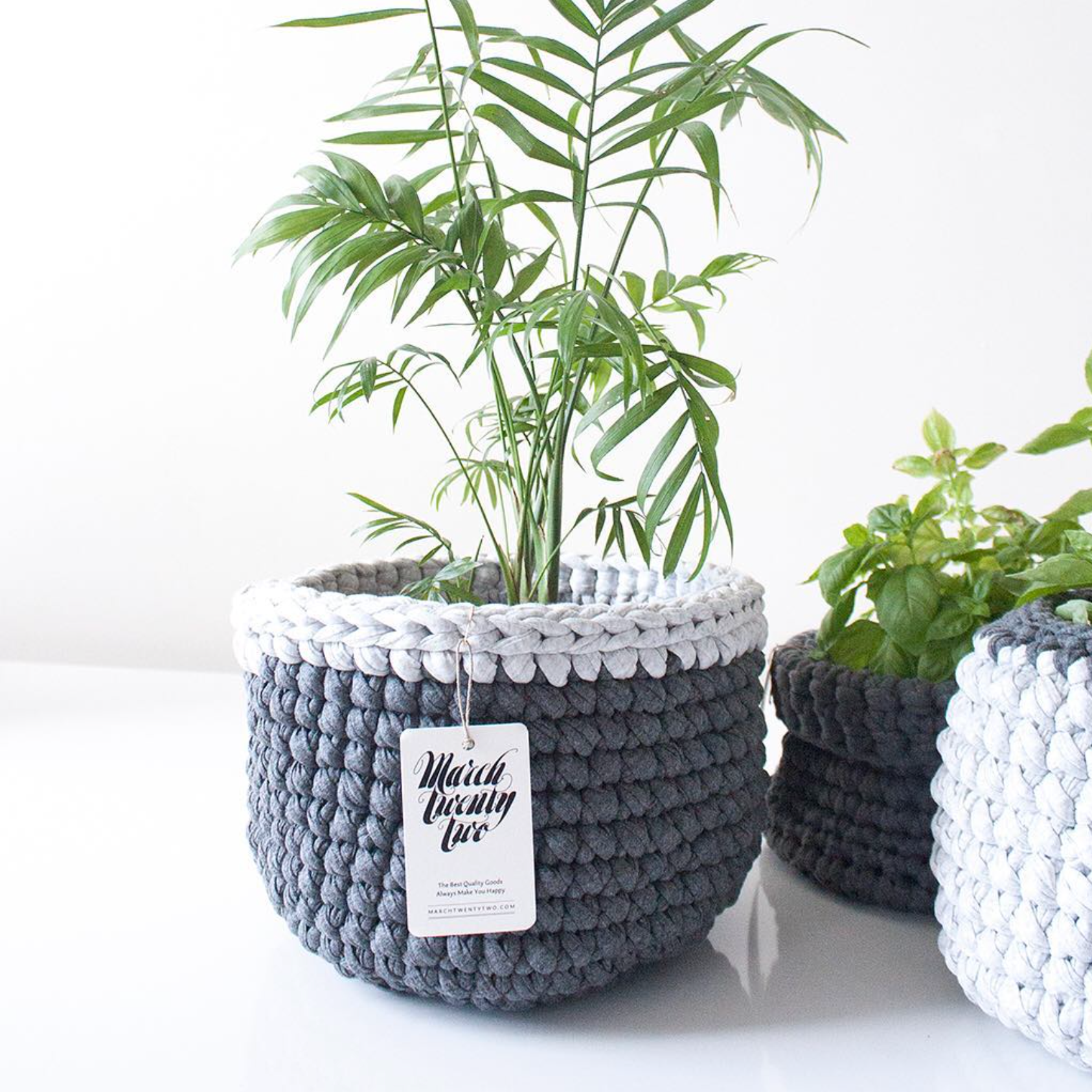 White and gray crocheted plant baskets with potted green plants on a bright windowsill.
