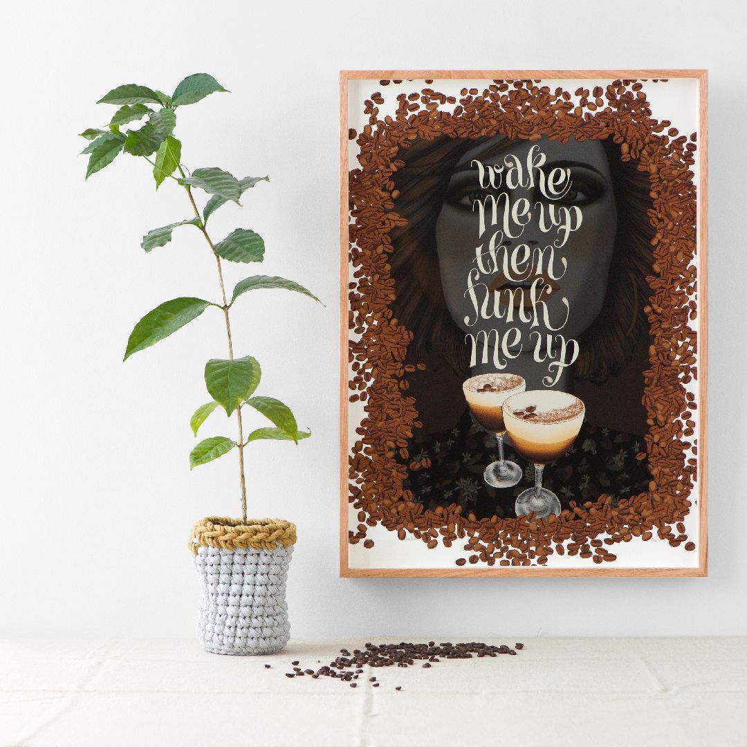 Potted plant beside a framed brown-toned wall art print with decorative lettering and a small drink photo