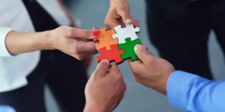 Several people holding puzzles pieces together