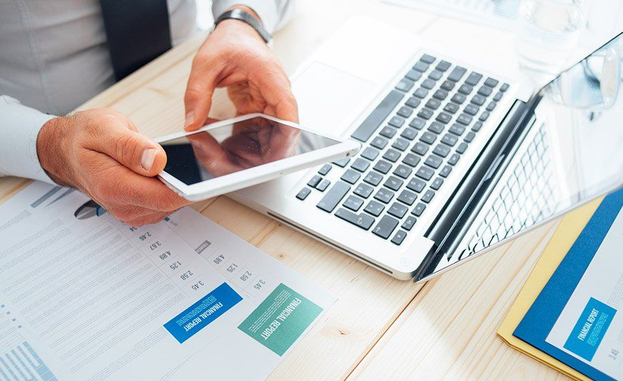 Person using a device surrounded by financial papers and laptop