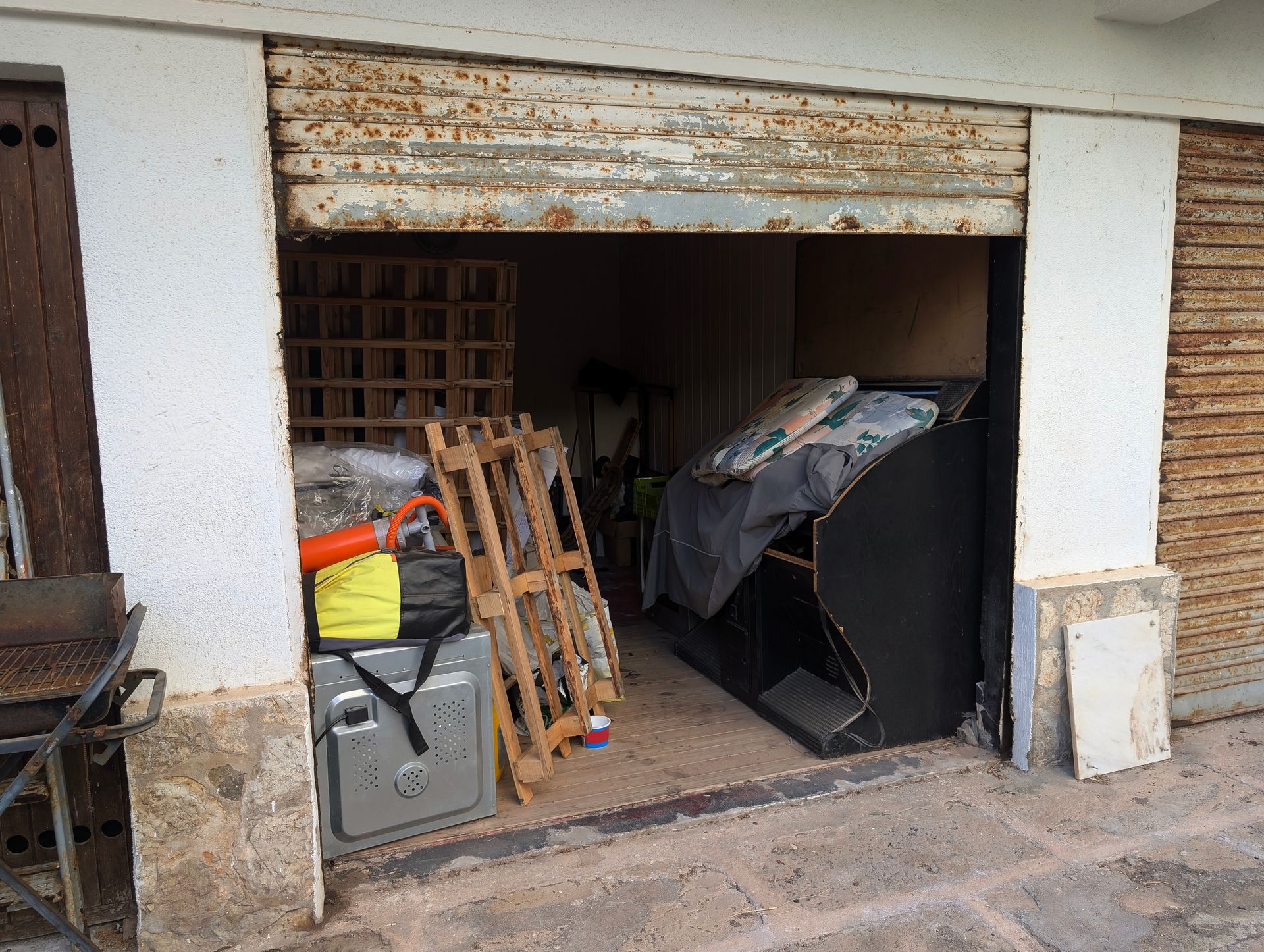 Open garage-style storage unit containing pallets, furniture, and stored items.