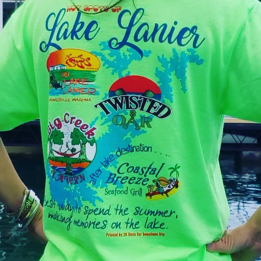 Bright green Lake Lanier T-shirt with colorful resort logos and text on a person by the water