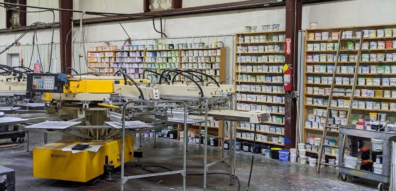 Industrial workshop with yellow machinery, metal racks, and shelves of parts in the background