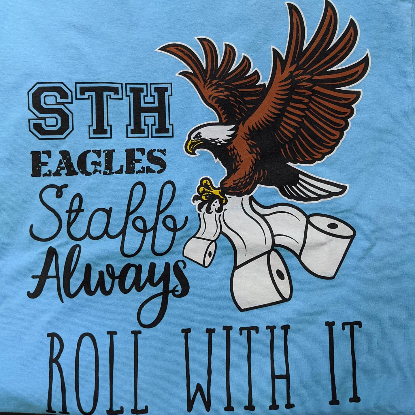 Blue shirt graphic with eagle, toilet paper rolls, and text “STH Eagles Staff Always Roll With It”