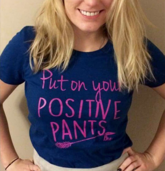 Person wearing a blue shirt with pink text that says “Put on your positive pants.”