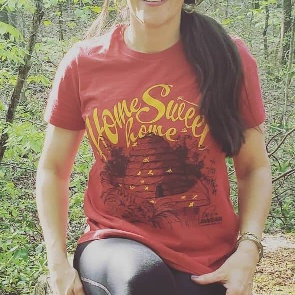 Person sitting outdoors in a red “Home Sweet Home” T-shirt with a ponytail.
