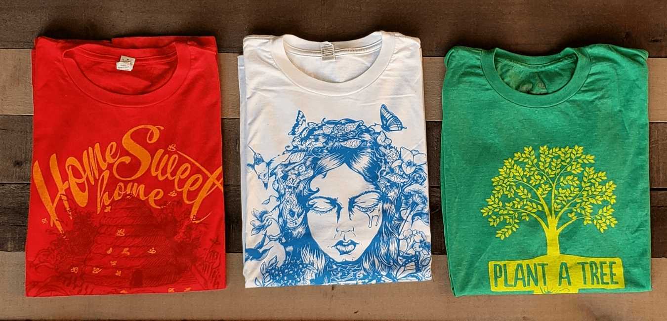 Three folded graphic T-shirts in red, white, and green with decorative prints.
