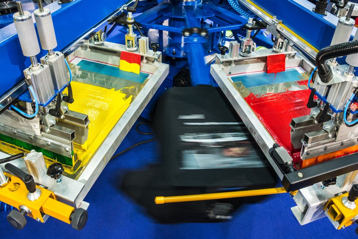 Machines screen printing t-shirts in different colors - outsource screen printing services.