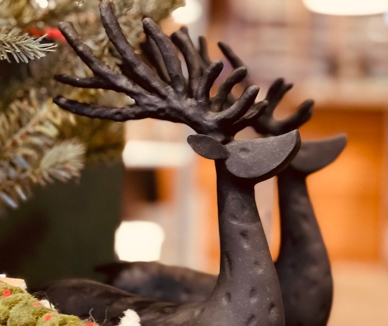 Two black decorative reindeer figurines beside a Christmas tree, softly lit indoors