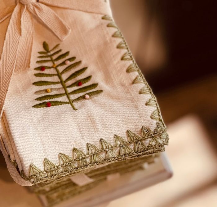 Embroidered linen napkin with a green tree design and stitched gold border on a stack of books
