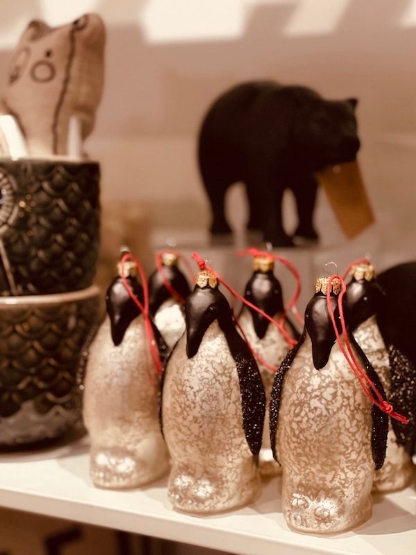 Small penguin figurines in a row with red scarves, with a dark elephant figurine blurred in the background.