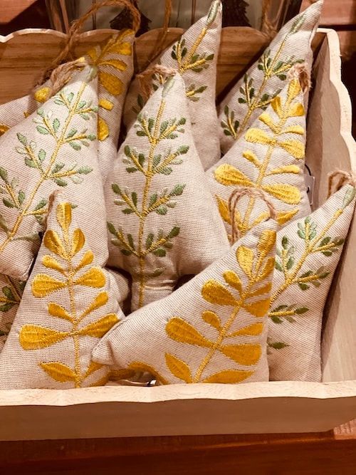 Embroidered white and mustard decorative fabric sachets arranged in a wooden tray