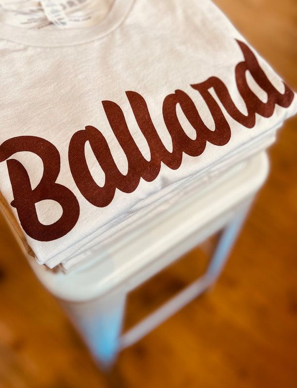 White cap with brown script “Ballard” on a clear container against a warm wooden floor.