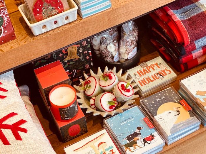 Holiday gift display with red-and-white sweets, candles, and “Happy Holidays” cards on a wooden shelf