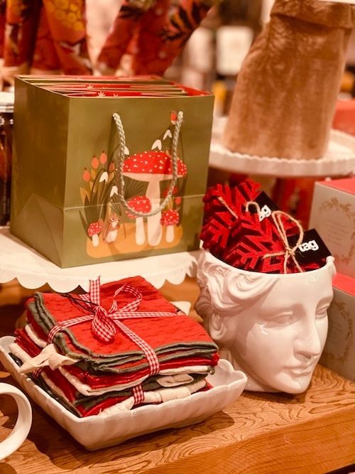 Holiday gift baskets and folded napkins on a wooden table, with a decorative white head planter holding red accents