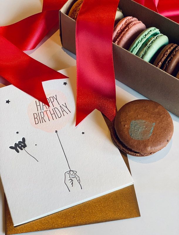 Birthday gift box with red ribbon, card, and assorted macarons on a table