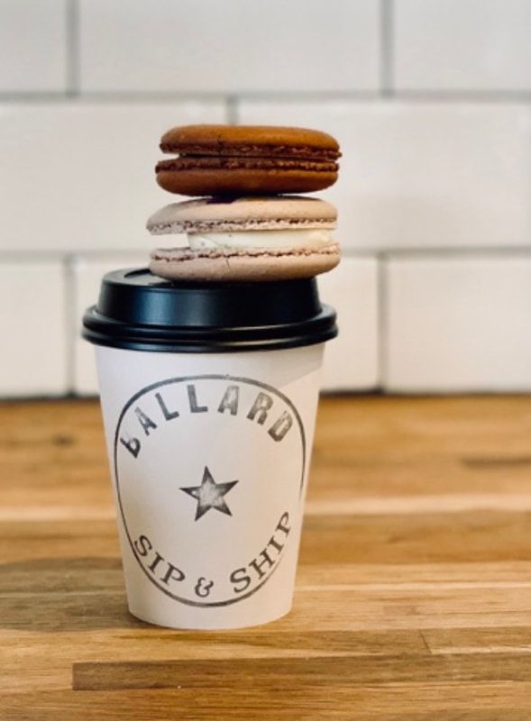 Coffee cup with black lid and two stacked macarons on top, on a wooden counter.