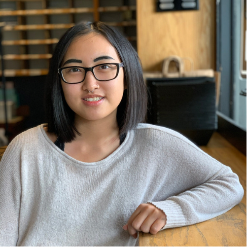 Woman with glasses smiling at a wooden table in a cozy indoor café