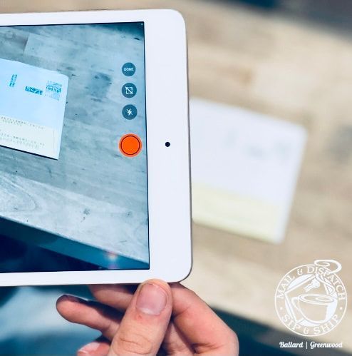 Tablet screen photographing a paper document on a desk, with an orange on-screen capture button