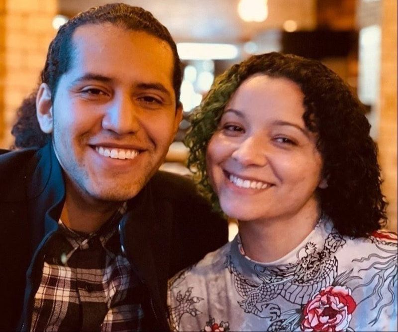 Two smiling people posing closely together in a warmly lit indoor setting.