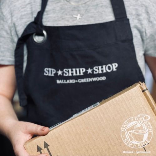 Person in a black apron holds a cardboard box with SIP SHIP SHOP logo