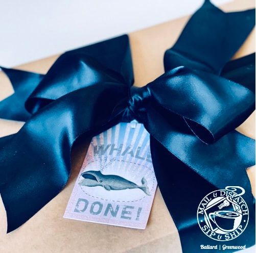 Gift box with a large navy satin bow and tag reading “WHALE DONE!” with a whale illustration.