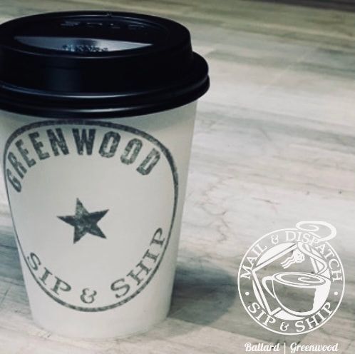 White coffee cup with black lid and green “GREENWOOD SIP & SHOP” logo on a table