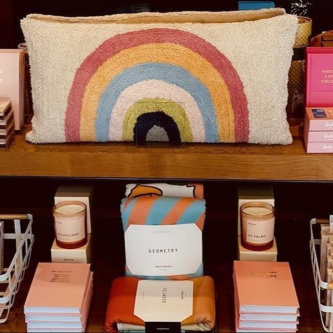Rainbow-decor pillow displayed on a shelf with candles and neatly stacked boxed goods