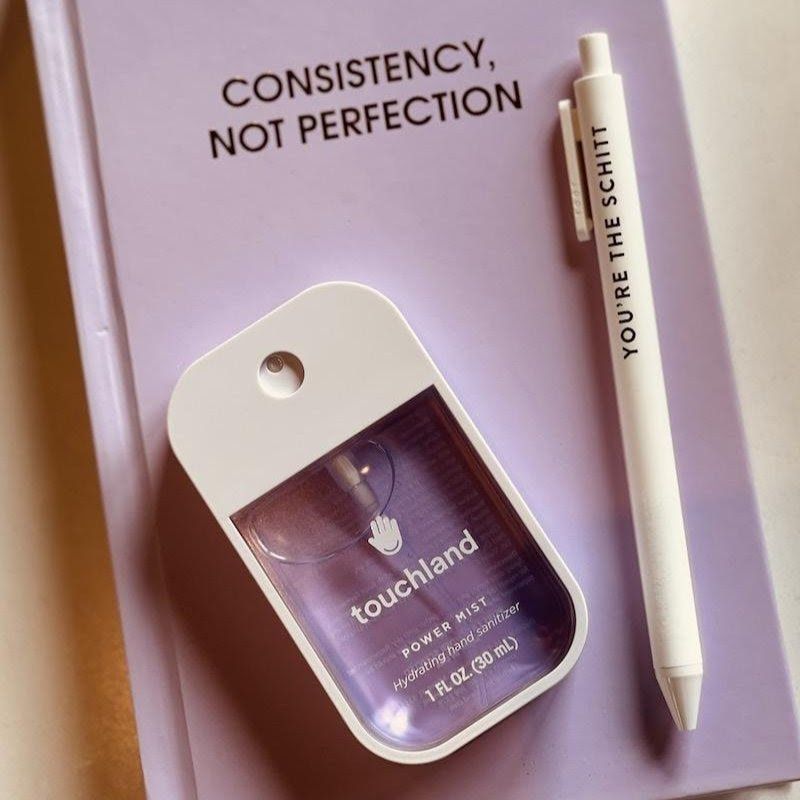 Lavender desk flat lay with a Touchland hand sanitizer, white pen, and “Consistency, not perfection” text