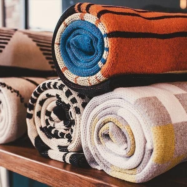 Rolled patterned blankets in orange, blue, black, and white on a wooden shelf