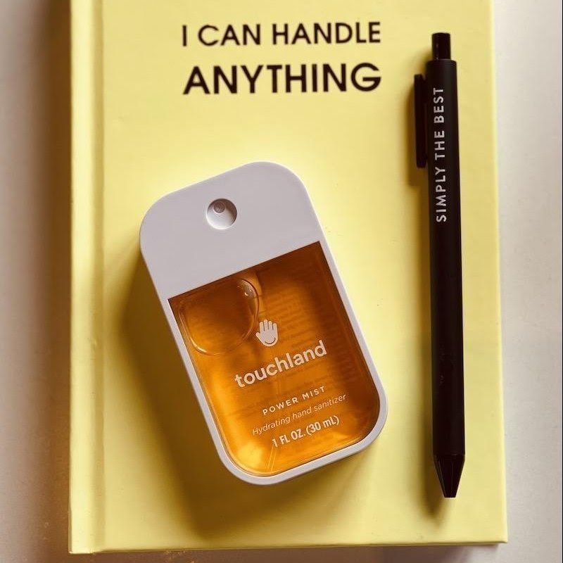 Yellow notebook with “I CAN HANDLE ANYTHING,” a Touchland hand sanitizer, and a black pen.