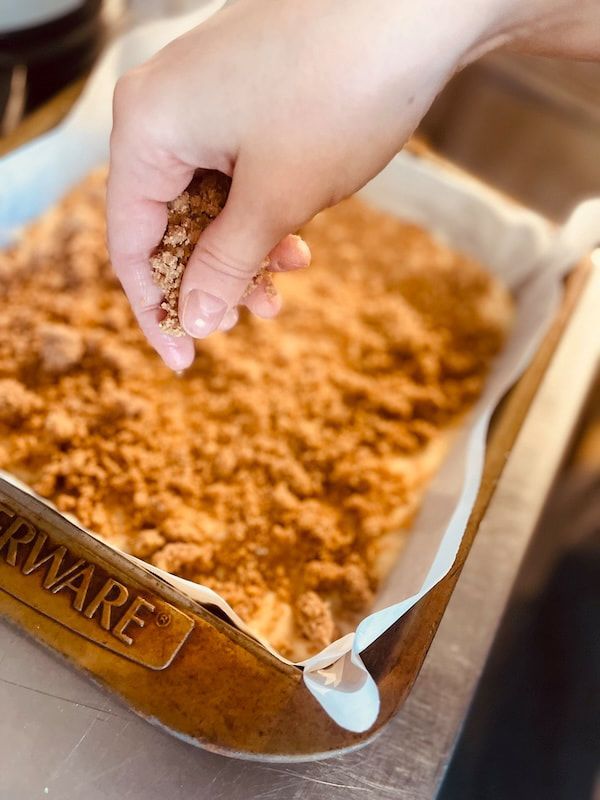 Hand sprinkling brown crumbs into a parchment-lined metal baking pan