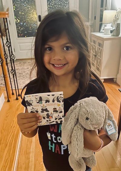 Smiling child holding a stuffed bunny and a small card in a living room