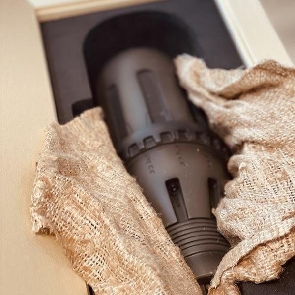 Black plastic nozzle wrapped in cloth inside a box with beige padding