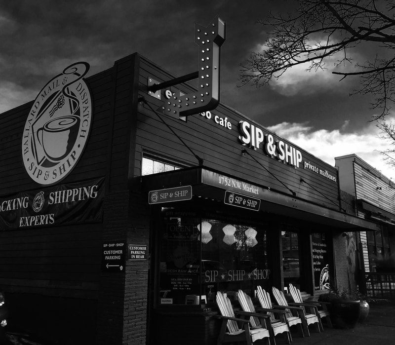 Black-and-white storefront for SIP & SHIP shipping supplies at dusk, with illuminated signs and outdoor displays