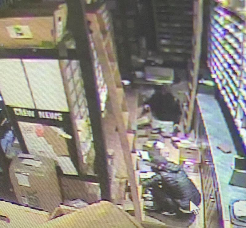 Overhead view of a cluttered store aisle with two people crouching among boxes and shelves