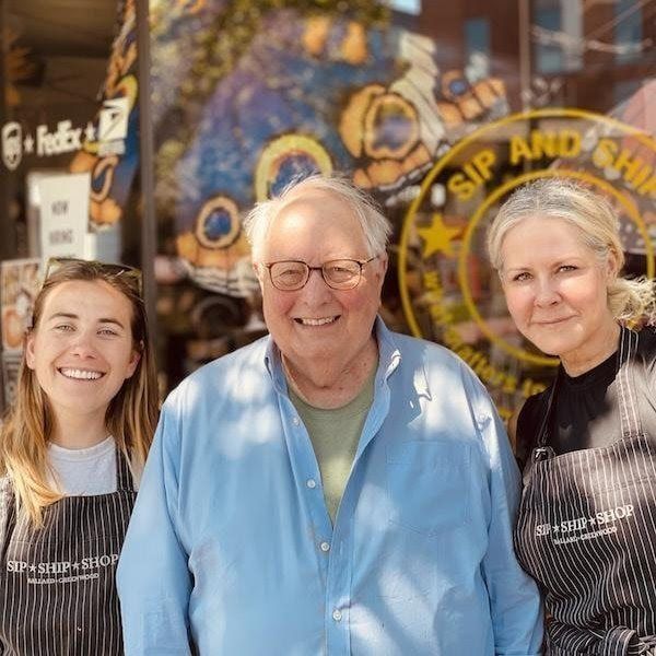 Three people smiling in front of a shop window and logo sign