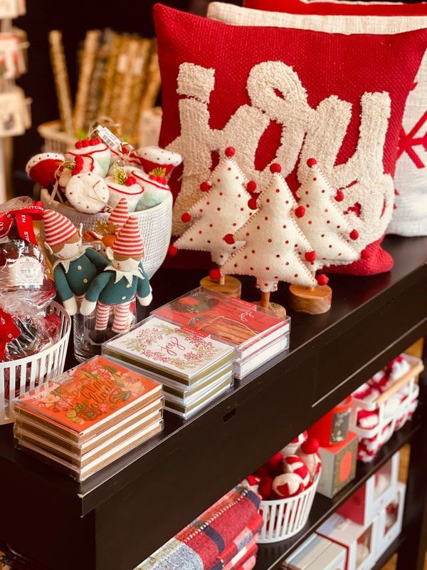 Holiday shelf display with red and white Christmas figurines, ornaments, and wrapped gift boxes