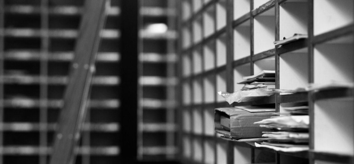 Black-and-white view of stacked papers on a shelf in a library or archive aisle