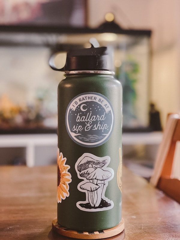 Green insulated water bottle with a black lid and mushroom sticker on a wooden table