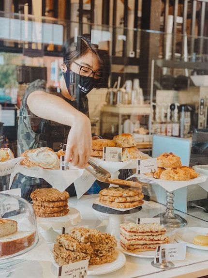 Bakery display with assorted pastries as a masked worker arranges baked goods behind the counter