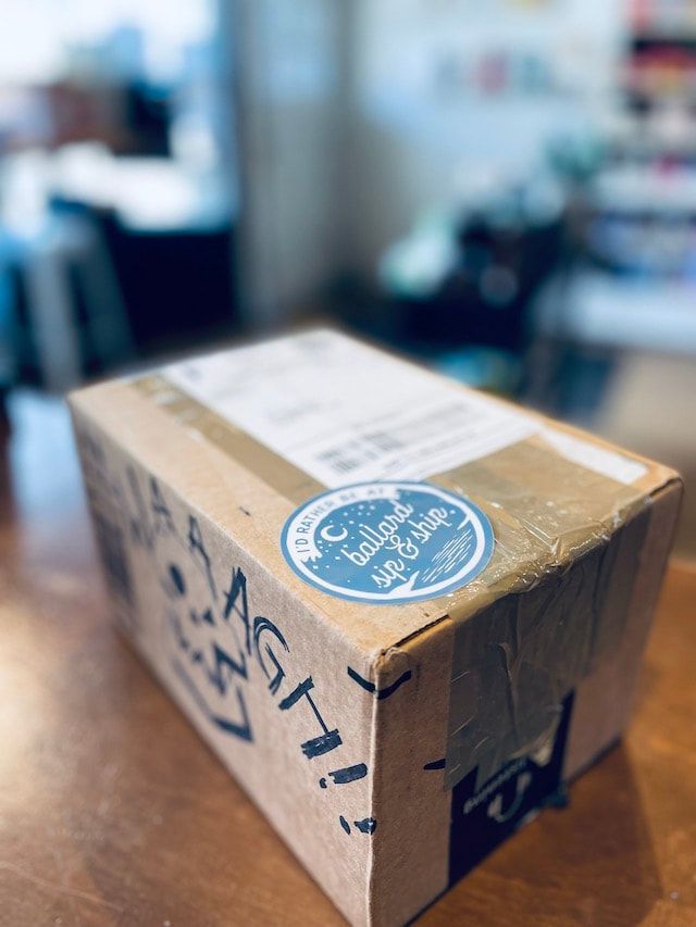 Cardboard shipping box with blue sticker on a wooden table in a blurred indoor setting
