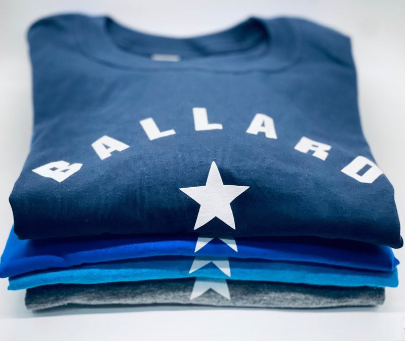 Stack of folded blue Ballard T-shirts with a white star logo on top