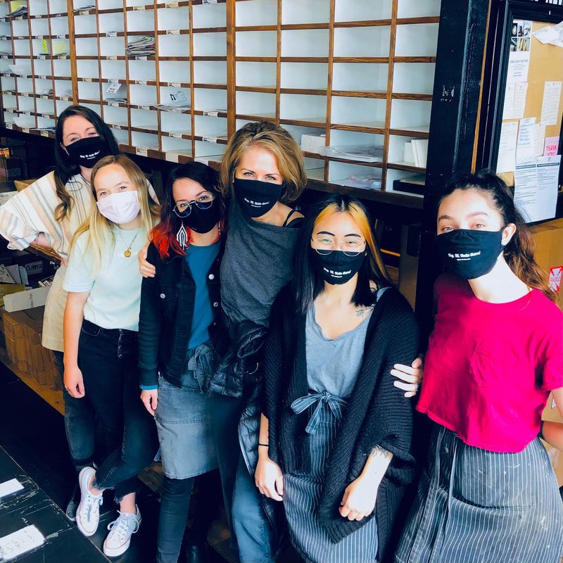 Six masked people posing together indoors in front of a wooden lattice wall