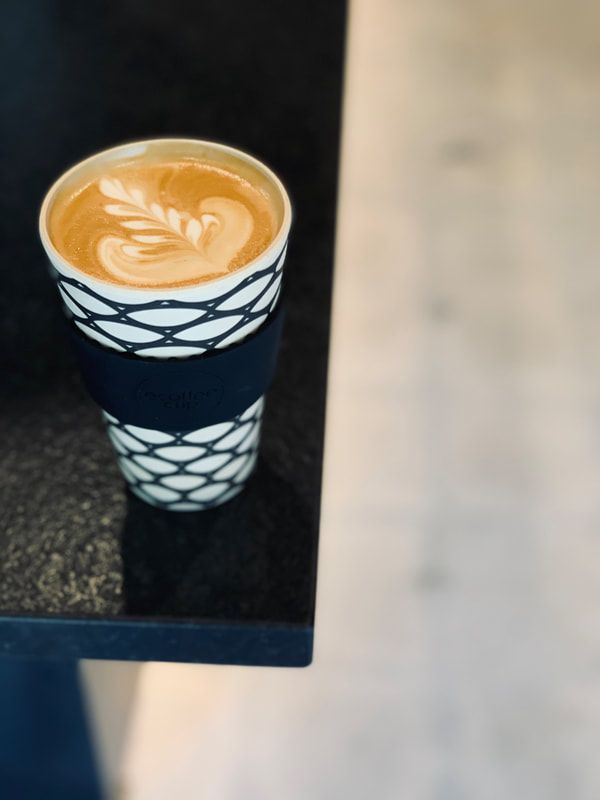 Tall patterned cup of latte with heart-shaped foam on a dark table next to a light wall